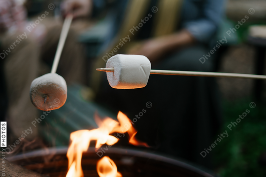 Black friends gathering around fire-pit roasting marshmallows and eating smores