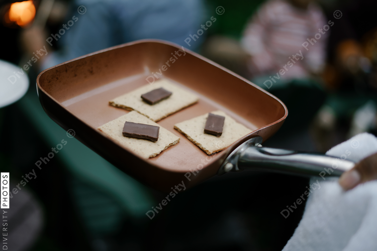 Black friends gathering around fire-pit roasting marshmallows and eating smores