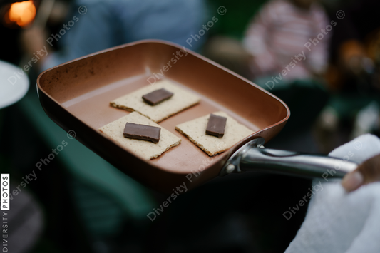 Black friends gathering around fire-pit roasting marshmallows and eating smores