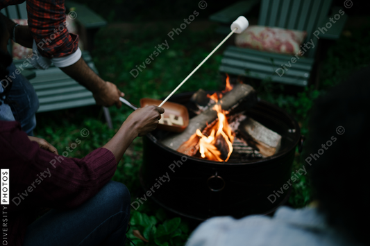 Black friends gathering around fire-pit roasting marshmallows and eating smores