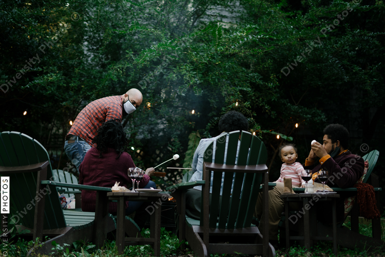 Black friends gathering around fire-pit roasting marshmallows and eating smores