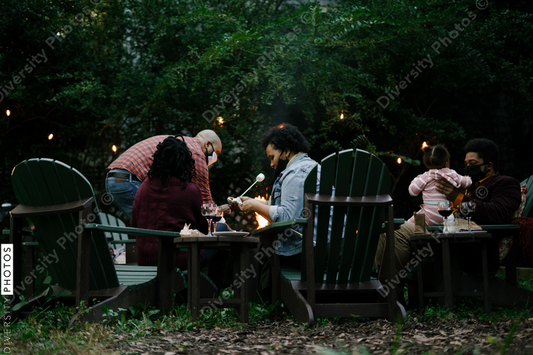 Black friends gathering around fire-pit roasting marshmallows and eating smores