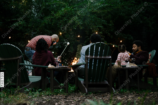 Black friends gathering around fire-pit roasting marshmallows and eating smores having a good time
