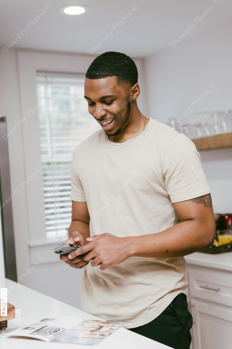Black man checks phone in kitchen at home