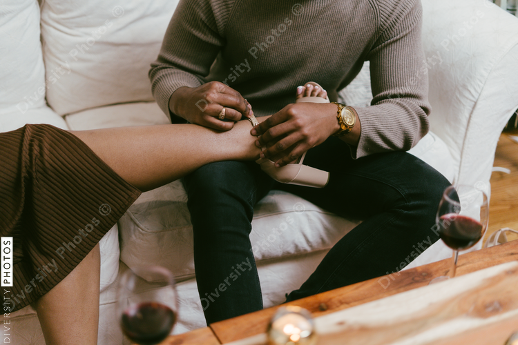 Man helps girlfriend take off shoes to relax on couch at home