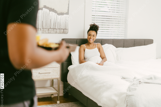 Black man bringing breakfast to girlfriend in bed at home
