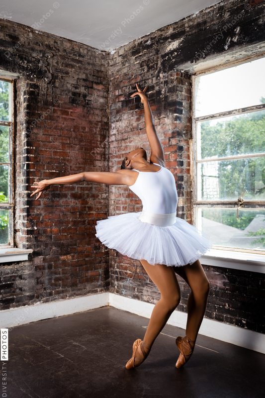 Black ballerina doing powerful ballet dance pose, wearing pointe shoes and white tutu, perseverance 