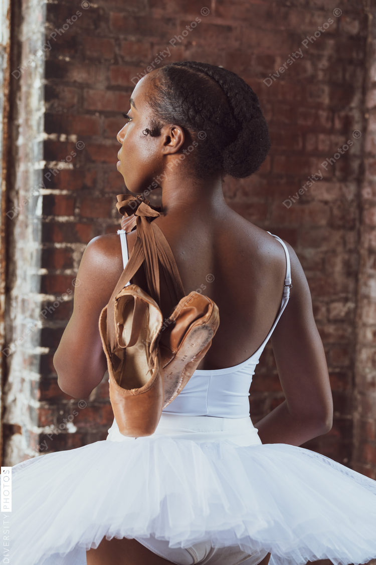 Portrait of attractive Black woman, ballerina dancer wearing tutu and holding pointe shoes