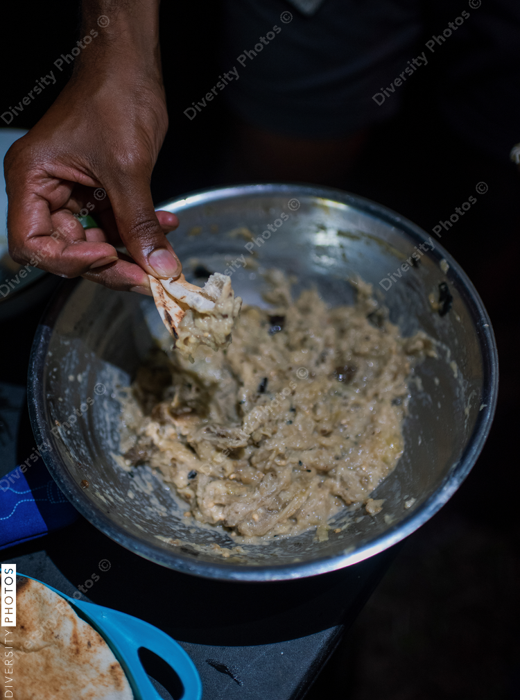 Close up of mans hand holding flatbread, reaching for spread in bowl