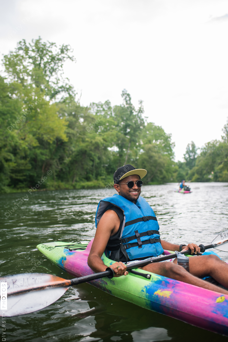 Portrait of smiling man in sunglasses sitting in colorful kayak on river