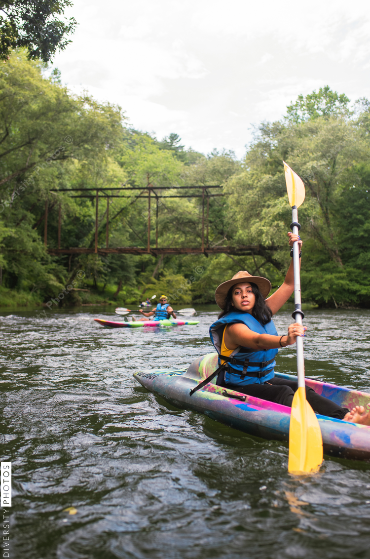 Woman and man kayaking on river with trees and footbridge in background