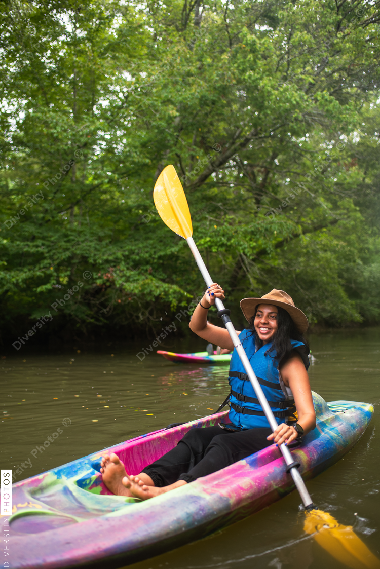 Smiling woman kayaking on river surrounded with trees