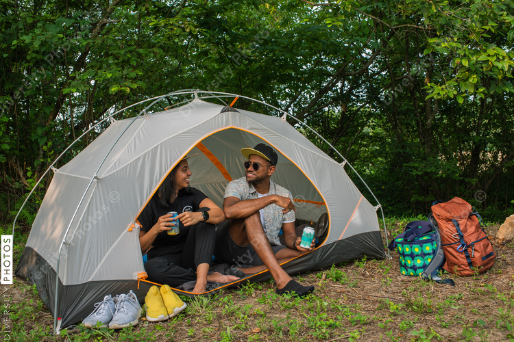 Smiling couple sitting in tent, holding canned drinks