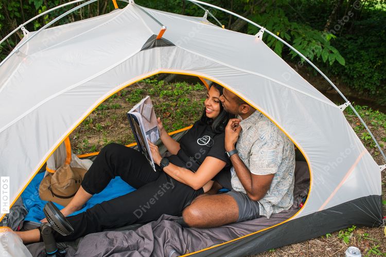 Smiling couple sitting in tent, reading book together