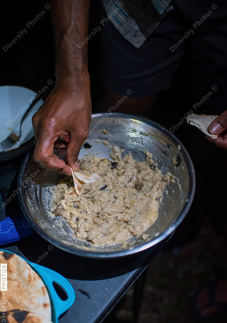 Close up of mans hand holding flatbread, reaching for spread in bowl