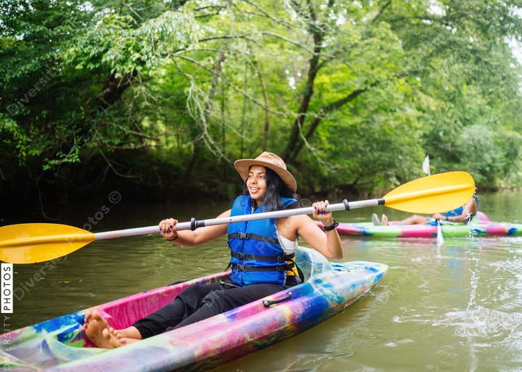 Smiling woman kayaking on calm river surrounded with trees in colorful kayak