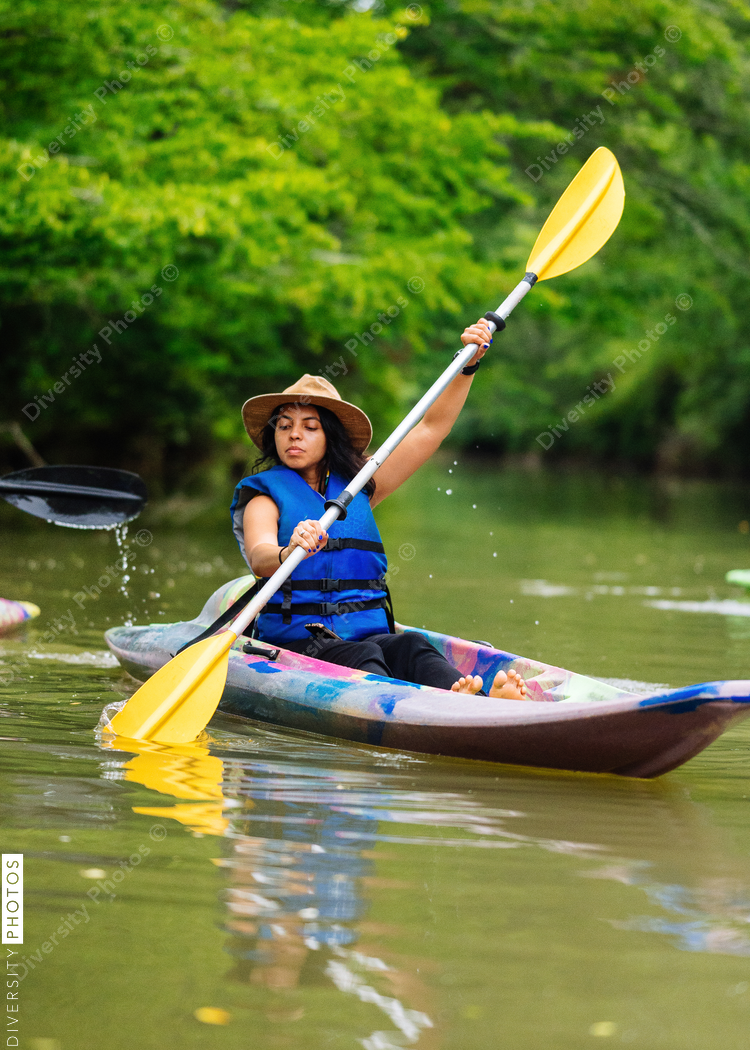 Woman in colorful kayak paddling on calm green river surrounded with trees