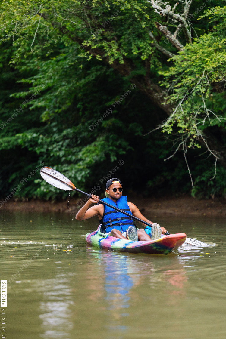 Man in colorful kayak on calm river with trees in background