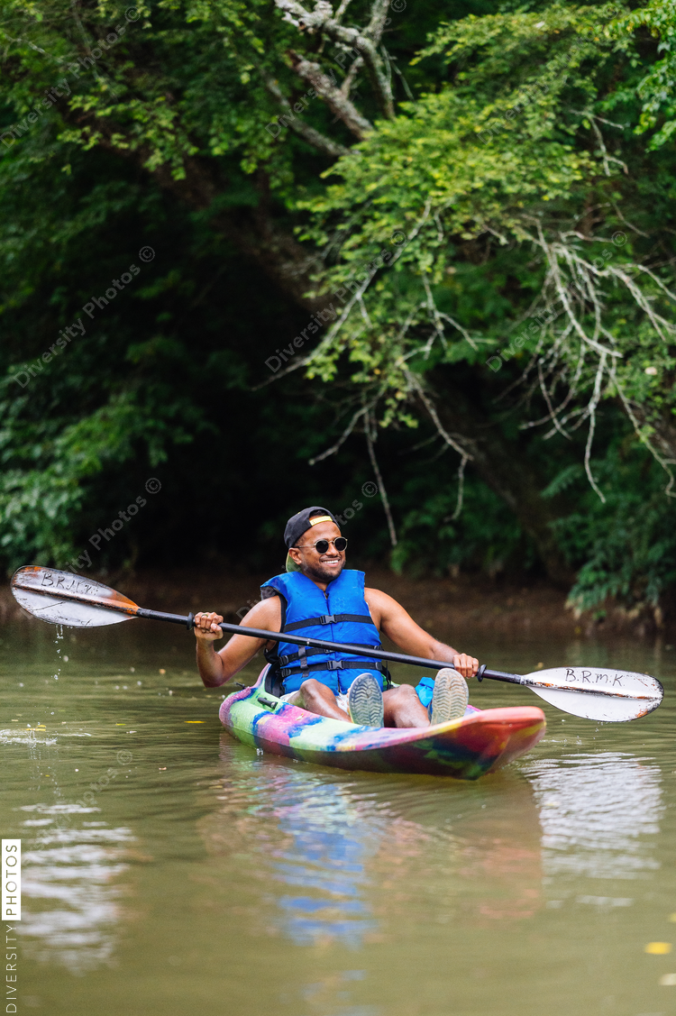 Smiling man in colorful kayak on calm river with trees in background