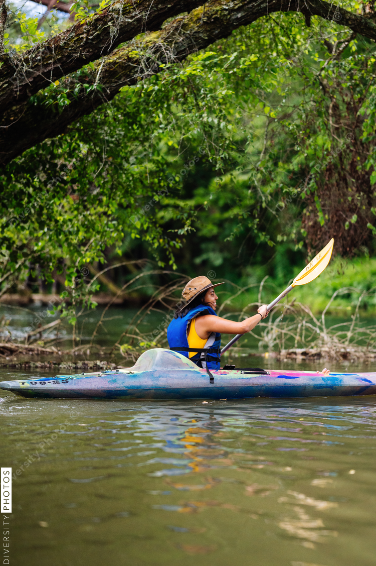Woman in hat kayaking on calm river with trees in background