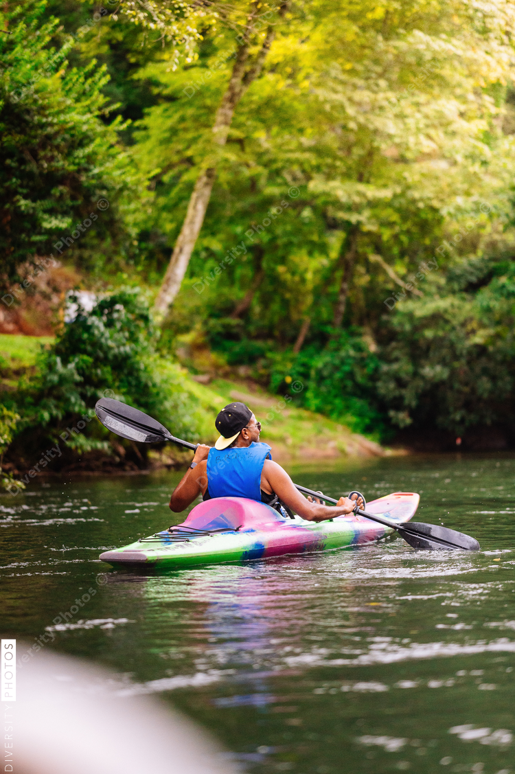 Rear view of man in colorful kayak on calm river surrounded with trees