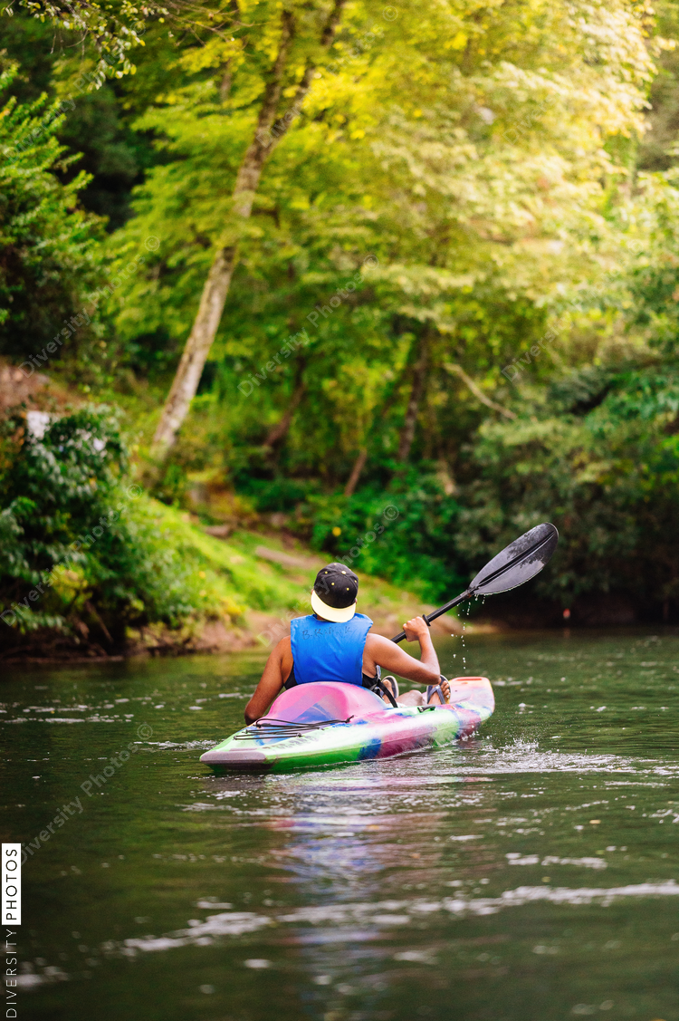 Rear view of man in colorful kayak on calm river surrounded with trees