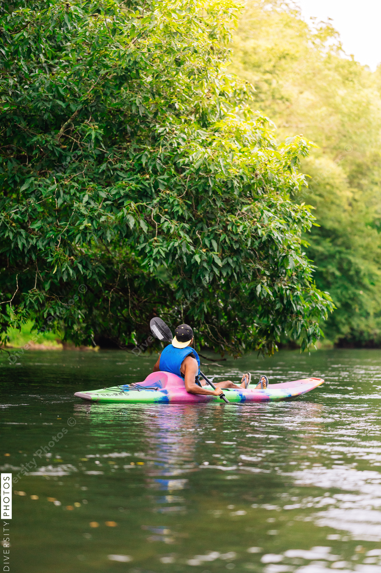 Man in colorful kayak on calm river surrounded with trees