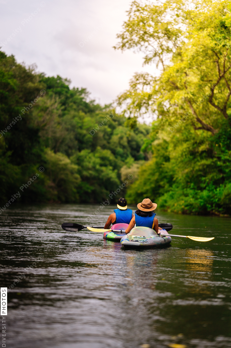 Rear view of people kayaking on calm river surrounded with trees
