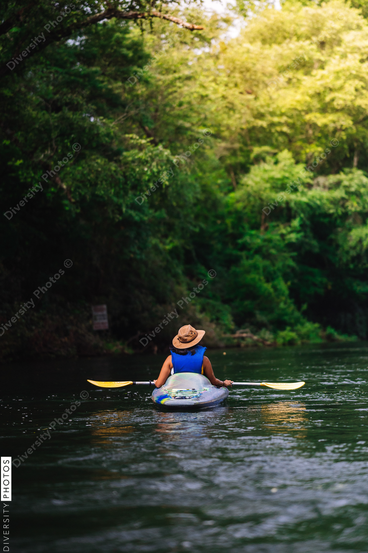 Rear view of woman in hat kayaking on calm river surrounded with trees