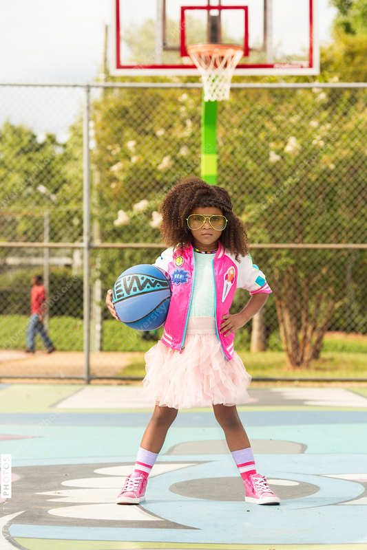 Young girl poses on basketball court with basketball and tutu