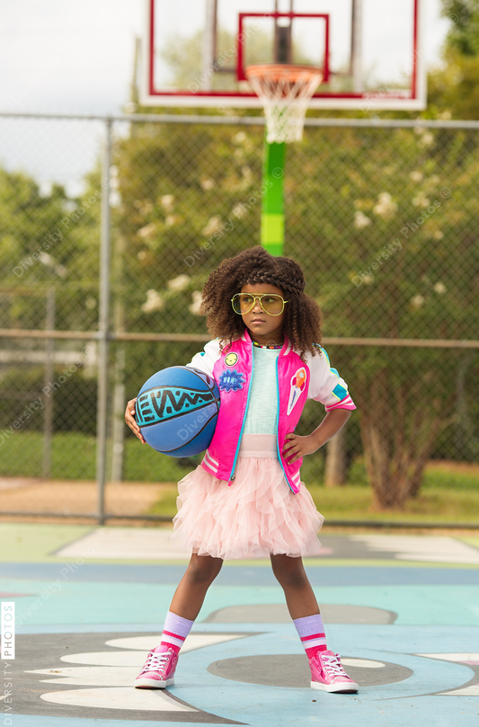 Young girl poses on basketball court with basketball and tutu