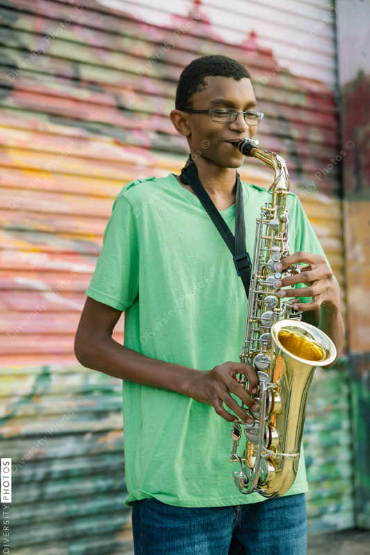 Black teenager practicing saxophone at school on colorful background