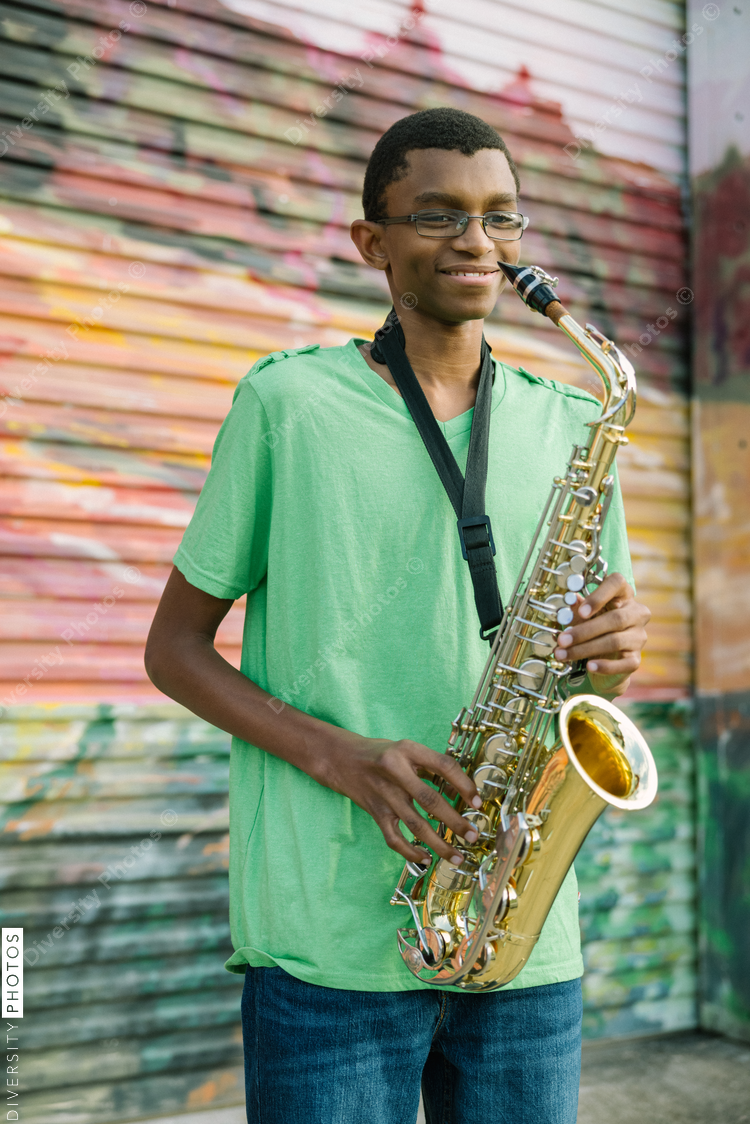 Talented Black teenager practicing saxophone at school on colorful background
