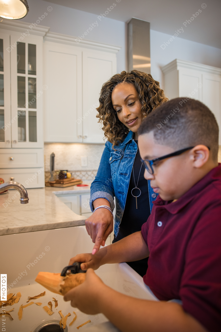 Black mother peeling potato with son in kitchen