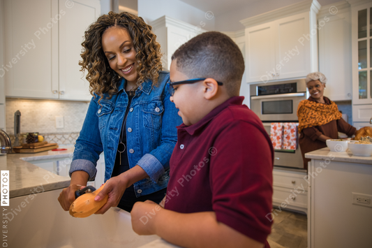 Black mother peeling potato with son in kitchen