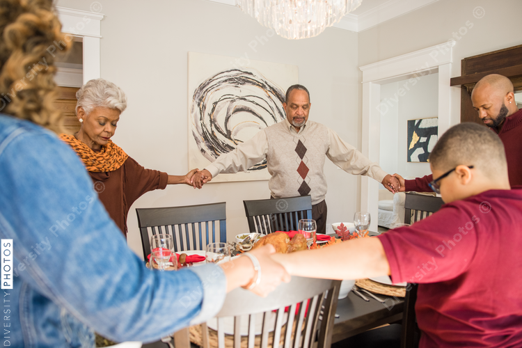 Black multigenerational family praying and blessing the food for Thanksgiving holiday meal
