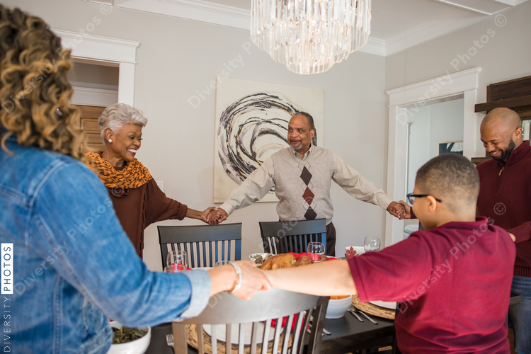 Black multigenerational family praying and blessing the food for Thanksgiving holiday meal