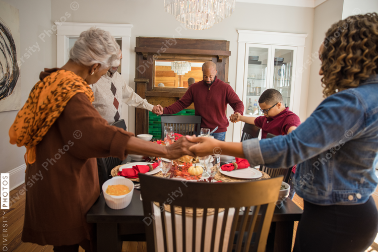 Black multigenerational family praying and blessing the food for Thanksgiving holiday meal