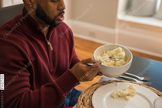 Black dad puts southern food on plate for Thanksgiving meal