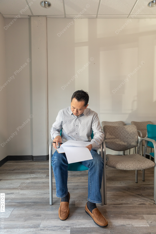 Asian man filling out patient forms at doctors office waiting area