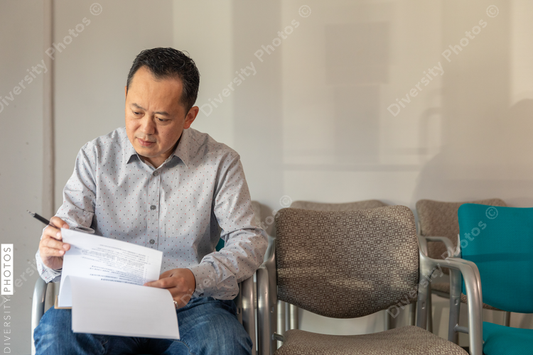 Asian man filling out patient forms at doctors office waiting area