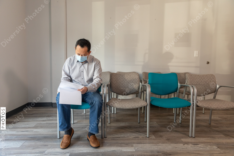 Asian man filling out patient forms at doctors office waiting area