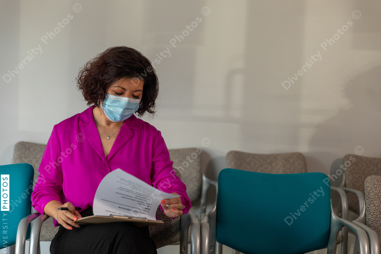 Asian woman completes patient forms in doctors lobby waiting room