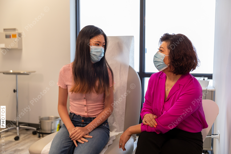 Mother and daughter waits to see doctor in medical exam room with mask