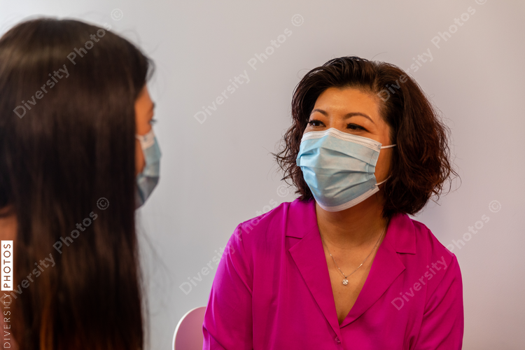 Mother and daughter waits to see doctor in medical exam room with mask