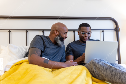 Black gay couple working in bed together, at home remotely