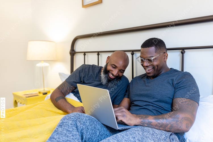 Black gay couple working in bed together, at home remotely