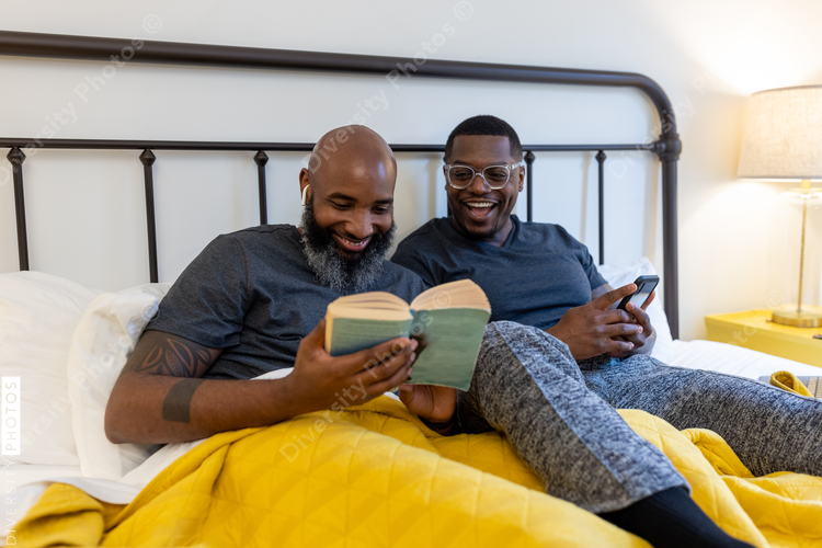 African American gay couple working and reading in bed at home, LGBTQ love