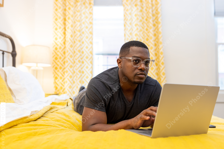 Black man working from home on laptop in bed