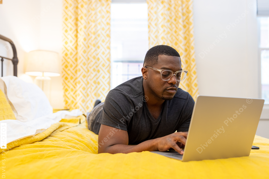 Black man working from home on laptop in bed